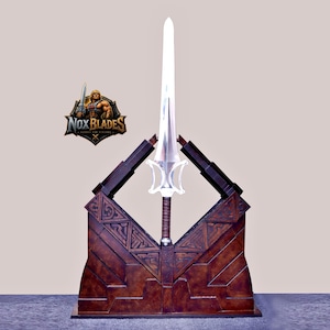 May include: A silver-colored sword with a distinctively shaped guard and a brown wrapped handle, displayed vertically in a dark brown, angular, textured stand. A logo featuring a muscular figure and the text NOX BLADES is visible.