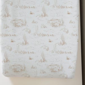 May include: A light blue fitted sheet with a delicate brown pattern of stylized plants and animals. The pattern is repeated throughout the sheet.