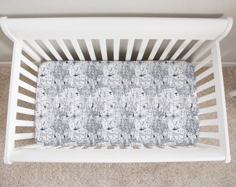 May include: A white cot with a mattress displaying a map-like design in grey and navy blue. The cot has a slatted design and curved headboard and footboard. The cot is on a beige carpet.