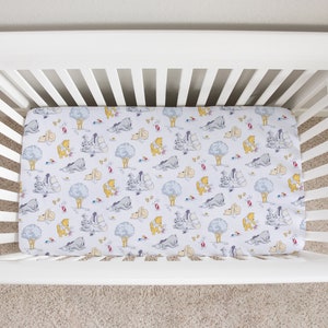 May include: A white cot with a fitted sheet featuring a Winnie the Pooh and friends print. The sheet has a light blue background with yellow, grey, and brown characters.