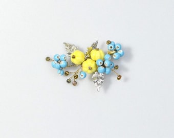 May include: A decorative brooch featuring three small yellow pumpkin-shaped elements surrounded by clusters of light blue spherical beads and silver-toned metallic leaves, all connected by thin, flexible gold-colored wire stems.
