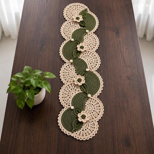Peut inclure: Un chemin de table rectangulaire en crochet composé d'un motif répétitif de napperons circulaires beiges et de segments semi-circulaires vert foncé. Le chemin est orné de petites fleurs beiges en relief et de perles rondes au centre.