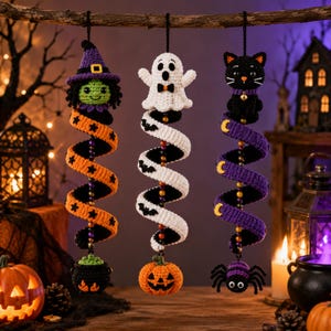 Op de afbeelding: Drie hangende gehaakte Halloween-decoraties met een heks met een ketel, een spook met een pompoen en een zwarte kat met een spin. Elk ornament heeft een spiraalvormig lichaam met kleurrijke kralen en feestelijke patronen zoals sterren.
