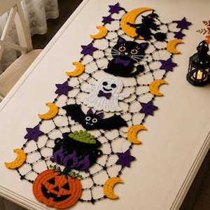May include: A rectangular Halloween-themed crochet table runner featuring a black web pattern adorned with crocheted motifs including a pumpkin, a cauldron, a bat, a ghost, a black cat, and a witch on a moon, accented by yellow moons and purple stars.