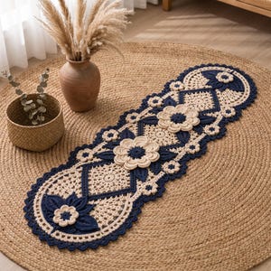 Puede incluir: Un camino de mesa ovalado y alargado con intrincado trabajo de ganchillo en color crema y azul marino. El diseño incorpora motivos florales en relieve con pétalos superpuestos y patrones de encaje geométrico, con un borde festoneado.