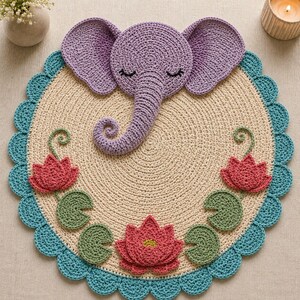 May include: A round crochet mat featuring a central purple elephant head with closed eyes and a trunk. The beige circular base is decorated with three pink lotus flowers and green lily pads, finished with a scalloped teal blue border edge.