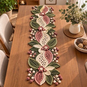 May include: A long, rectangular crochet table runner featuring a repeating botanical pattern of dark green leaves, cream-colored lace-like sections, dusty pink petal shapes, and clusters of small white and pink berries arranged in a line.
