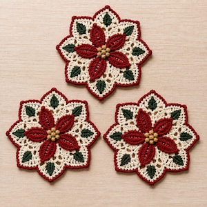 Puede incluir: Tres posavasos de ganchillo circulares con un diseño de flor de pascua. Cada posavasos tiene una base de encaje color crema, hojas verde oscuro, pétalos rojo intenso y un grupo de pequeñas cuentas de color marrón claro en el centro.