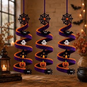 Puede incluir: Tres decoraciones en espiral colgantes hechas de tela de ganchillo morada y naranja. Cada una presenta una telaraña negra en la parte superior y figuras de ganchillo colgantes que incluyen un murciélago, un fantasma, una casa encantada, una calabaza y una araña negra.