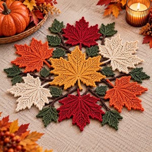 Peut inclure: Un napperon en crochet circulaire composé d'un ensemble de feuilles d'érable entrelacées dans des tons de rouge, orange, jaune et crème, agrémenté de petites feuilles vert foncé et de tiges brunes, formant un centre de table textile détaillé.