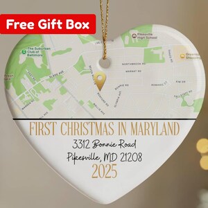 May include: Heart-shaped Christmas ornament with a map design and the text "FIRST CHRISTMAS IN MARYLAND". The ornament includes an address and the year 2025. A gold string is attached for hanging. The words "Free Gift Box" are in a red box.