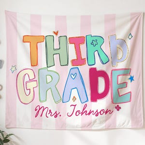 May include: A classroom banner with the words "THIRD GRADE" in colorful, playful letters. The banner is pink and white striped, with the name "Mrs. Johnson" written below. The banner is hanging in a classroom setting with desks and decor.