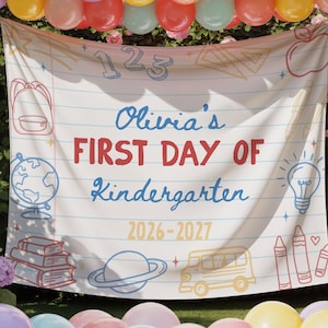 May include: A banner reading "Olivia's FIRST DAY OF Kindergarten 2026-2027" is shown, decorated with school-themed illustrations. It's surrounded by colourful balloons and flowers, creating a festive atmosphere.