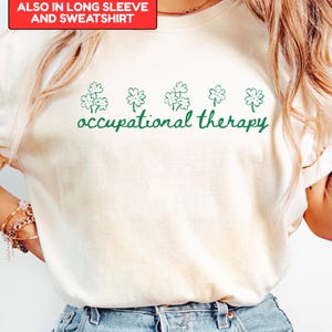 May include: Ivory-colored t-shirt with the words "occupational therapy" in green script, accompanied by green shamrock graphics. The shirt is also available in long sleeve and sweatshirt styles.
