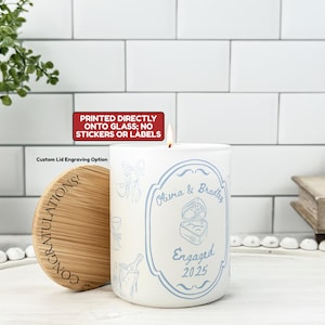 May include: A white candle with a blue design and the words "Olivia & Bradley Engaged 2025." The candle has a wooden lid with the word "CONGRATULATIONS!" printed on it. The candle is printed directly onto the glass.