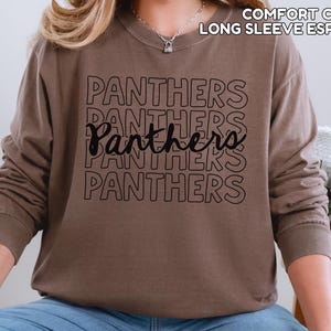 May include: Espresso-colored long-sleeve shirt with the word "Panthers" printed in black multiple times. The shirt has a crew neck and a relaxed fit. The text "COMFORT COLORS LONG SLEEVE ESPRESSO" is printed at the top.