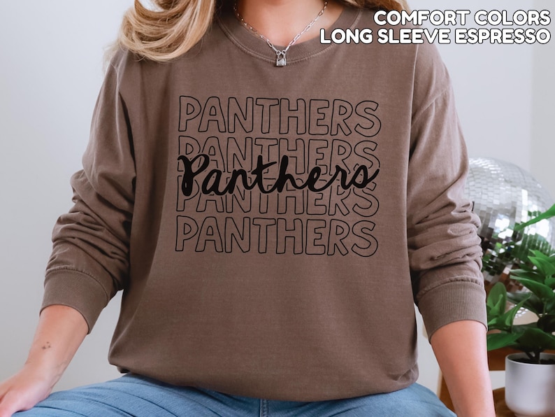 May include: Espresso-colored long-sleeve shirt with the word "Panthers" printed in black multiple times. The shirt has a crew neck and a relaxed fit. The text "COMFORT COLORS LONG SLEEVE ESPRESSO" is printed at the top.