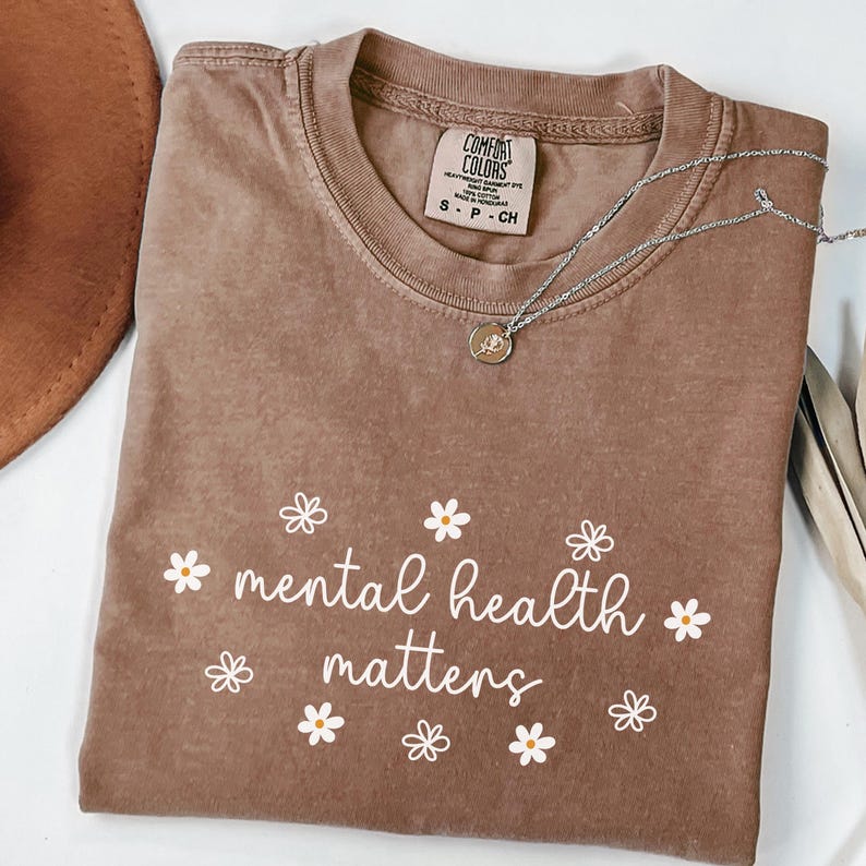 May include: A brown t-shirt with the text "mental health matters" in white lettering with small white daisy flowers surrounding the text.