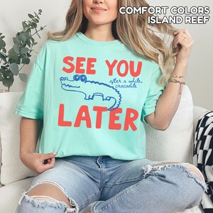 May include: A pale green t-shirt with the words "SEE YOU LATER" in red block letters. A blue cartoon crocodile is between the words. The text "after a while, crocodile" is above the crocodile.