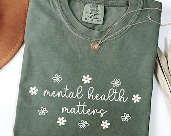 May include: A green t-shirt with the text "mental health matters" in white lettering with small white daisy flowers surrounding the text.