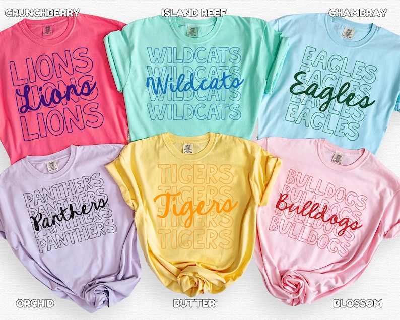 May include: A collection of six colorful t-shirts, each displaying a team name in a stacked design. Colors include pink, light blue, yellow, purple, and light pink. The text on the shirts reads "Lions", "Wildcats", "Eagles", "Panthers", "Tigers", and "Bulldogs".