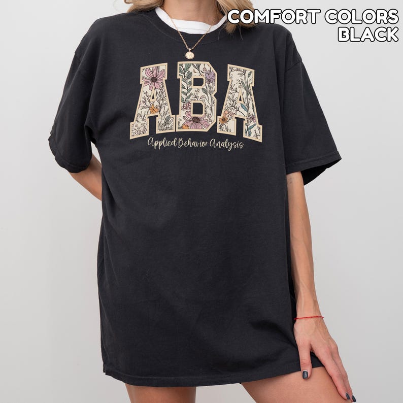 May include: Black t-shirt with the letters "ABA" in a floral design. The words "Applied Behavior Analysis" are printed below the letters. The shirt is a comfort colors style.