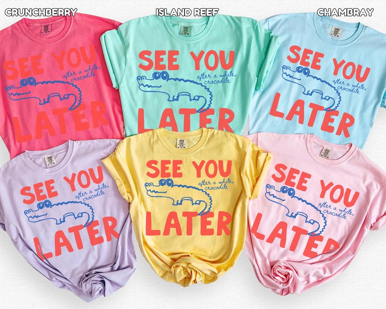 May include: A selection of t-shirts in various colours, including pink, blue, green, yellow, and purple. Each shirt displays the phrase "SEE YOU LATER" alongside a cartoon crocodile illustration. The text and crocodile are in contrasting colours.
