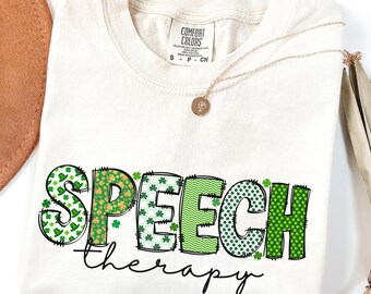 May include: A white t-shirt with the words "SPEECH therapy" in green, gold, and white shamrock patterns. The letters are outlined in black and have a stitched look.