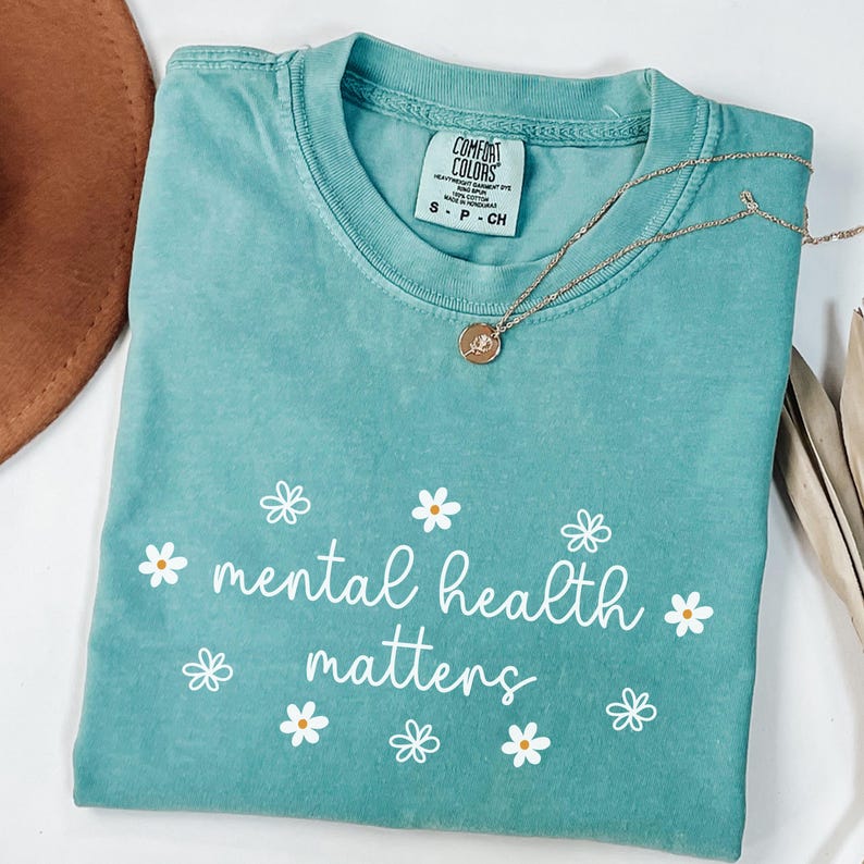 May include: A teal blue t-shirt with the text "mental health matters" in white lettering surrounded by white daisy flowers.
