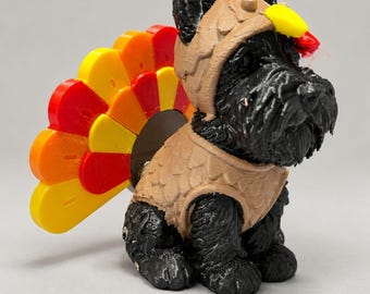 May include: A 3D-printed black dog figurine wearing a tan vest and a headpiece with a red crest and yellow beak. A fan-shaped tail attachment in alternating yellow, orange, and red segments is positioned behind the dog, mimicking a turkey.