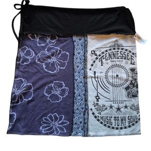 May include: A patchwork skirt with a black waistband and tie. The skirt features panels of dark purple fabric with white floral designs, a blue patterned panel, and a gray panel with a guitar graphic and the text "Tennessee Music to My Soul."