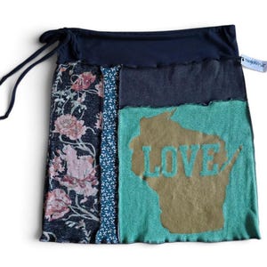 May include: A patchwork skirt featuring a dark navy waistband with tie strings, a floral print panel, a thin teal patterned strip, and a large teal section with a gold-colored map of Wisconsin and the word LOVE printed in teal letters.