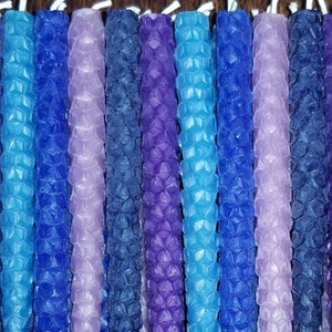 May include: A collection of hexagonal patterned candles in shades of blue, purple, and lavender. The candles are arranged in a row and are all the same size.