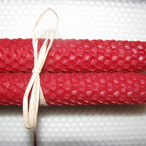 May include: Two red beeswax candles tied together with a natural raffia ribbon. The candles have a honeycomb pattern.
