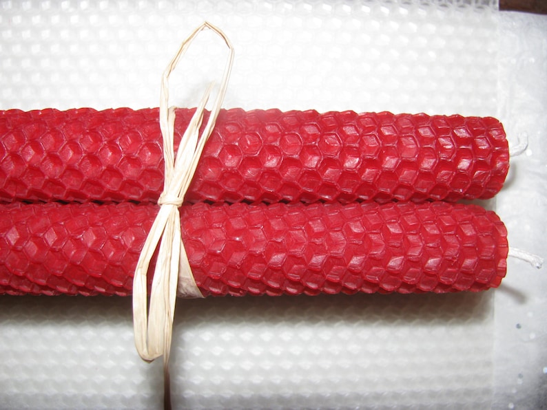 May include: Two red beeswax candles tied together with a natural raffia ribbon. The candles have a honeycomb pattern.