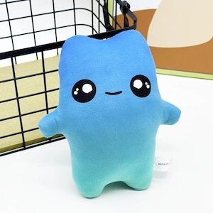 May include: A soft plush toy in a bright blue color with a gradient transition to a lighter teal at the base. The toy features a simple, rounded body shape with two small arms, a small embroidered smile, and two large black eyes with white highlights.