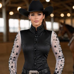 May include: A black long-sleeved shirt featuring sheer sleeves with intricate black beadwork, a high collar with black embellishments, and a central vertical row of black crystals. The shirt is paired with a black belt featuring a large silver buckle.