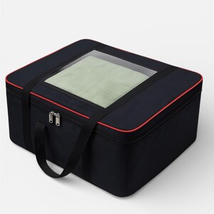 Puede incluir: Una bolsa de almacenamiento rectangular negra con una ventana de plástico transparente en la tapa superior, que revela una tela verde claro en el interior. La bolsa tiene un borde rojo, un cierre de cremallera y dos asas de tela negra.