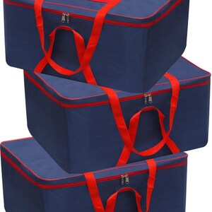 Puede incluir: Tres bolsas de almacenamiento rectangulares de tela azul marino con ribetes, cremalleras y asas de transporte en color rojo brillante. Cada bolsa presenta un diseño estructurado con tapa plana y una ventana rectangular transparente.