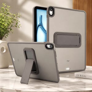 May include: Two tablet cases in a matte grey finish with a translucent back panel. Each case features a rectangular integrated kickstand on the rear, a camera cutout, and the word Pad printed on the lower section. One case is upright, showing the stand.