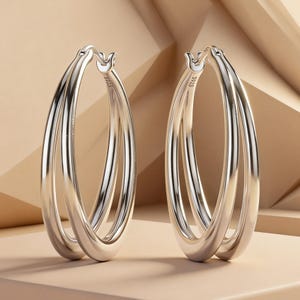 May include: A pair of silver hoop earrings featuring a double-layered design with a smooth, polished finish. Each earring is constructed from two interconnected circular bands that create a layered appearance, with the hallmark S925 visible.