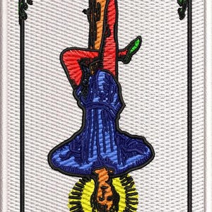 May include: A rectangular embroidered patch featuring The Hanged Man tarot card design. It depicts a figure hanging upside down from a brown wooden T-shaped structure with green foliage, wearing a blue tunic, red leggings, and green shoes, with a yellow halo.