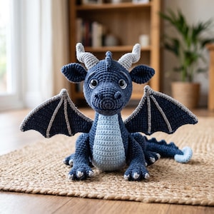 May include: A dark blue crocheted dragon toy featuring a light blue belly, two light gray horns, and wings with light gray accents. The creature has large dark eyes, a textured body, and a long tail with a light blue tip, crafted in yarn.