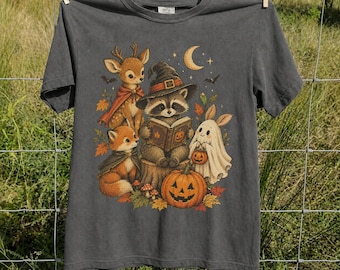 May include: A charcoal gray short-sleeve t-shirt featuring a graphic print of a raccoon wearing a witch hat and reading a book, a deer, a fox, a ghost, and a jack-o'-lantern, surrounded by autumn leaves, bats, and a crescent moon.