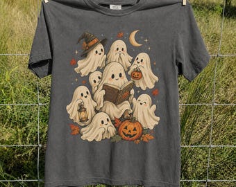 May include: A charcoal gray t-shirt featuring a graphic illustration of several white ghosts. One ghost wears a witch hat, one holds a lantern, one reads a book, and one sits beside a carved orange pumpkin. The design includes small stars and autumn leaves.