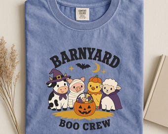 May include: A periwinkle blue t-shirt featuring a graphic of a cow in a witch hat, a pig in a mummy wrap, a chick in a pumpkin costume, and a sheep in a cape. The text reads BARNYARD BOO CREW above and below the animals with a jack-o'-lantern.