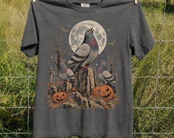 May include: A charcoal gray short-sleeve t-shirt featuring a graphic print of three pigeons perched on tombstones under a large full moon. The scene includes two orange jack-o'-lanterns, bare tree branches, and small bats against a dark night sky.