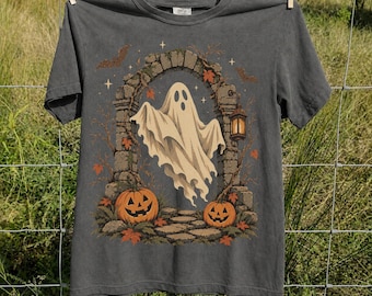 May include: A charcoal gray t-shirt featuring a graphic print of a white ghost floating under a stone archway. The design includes two orange jack-o'-lanterns, a hanging lantern, falling autumn leaves, and small stars against a dark background.