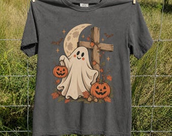 May include: A charcoal gray short-sleeve t-shirt featuring a graphic of a white ghost holding an orange jack-o'-lantern bucket. The design includes a wooden cross, a crescent moon, bats, stars, and autumn leaves in shades of orange and brown.