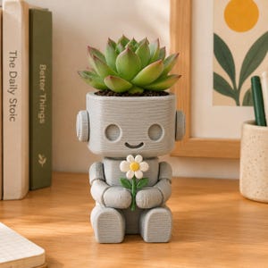 May include: A light gray robot-shaped planter with a textured finish, featuring a smiling face and round ears. The robot holds a small white flower with a yellow center and green stem. A green succulent plant is potted inside the robot's head.